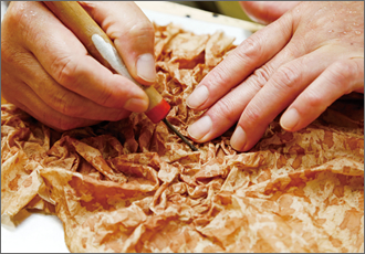 選りすぐった和紙を柿渋に浸し、錆（さび）と呼ばれる凹凸の皺を作る作業。均等な錆を作り出すには、熟練の技が必要。